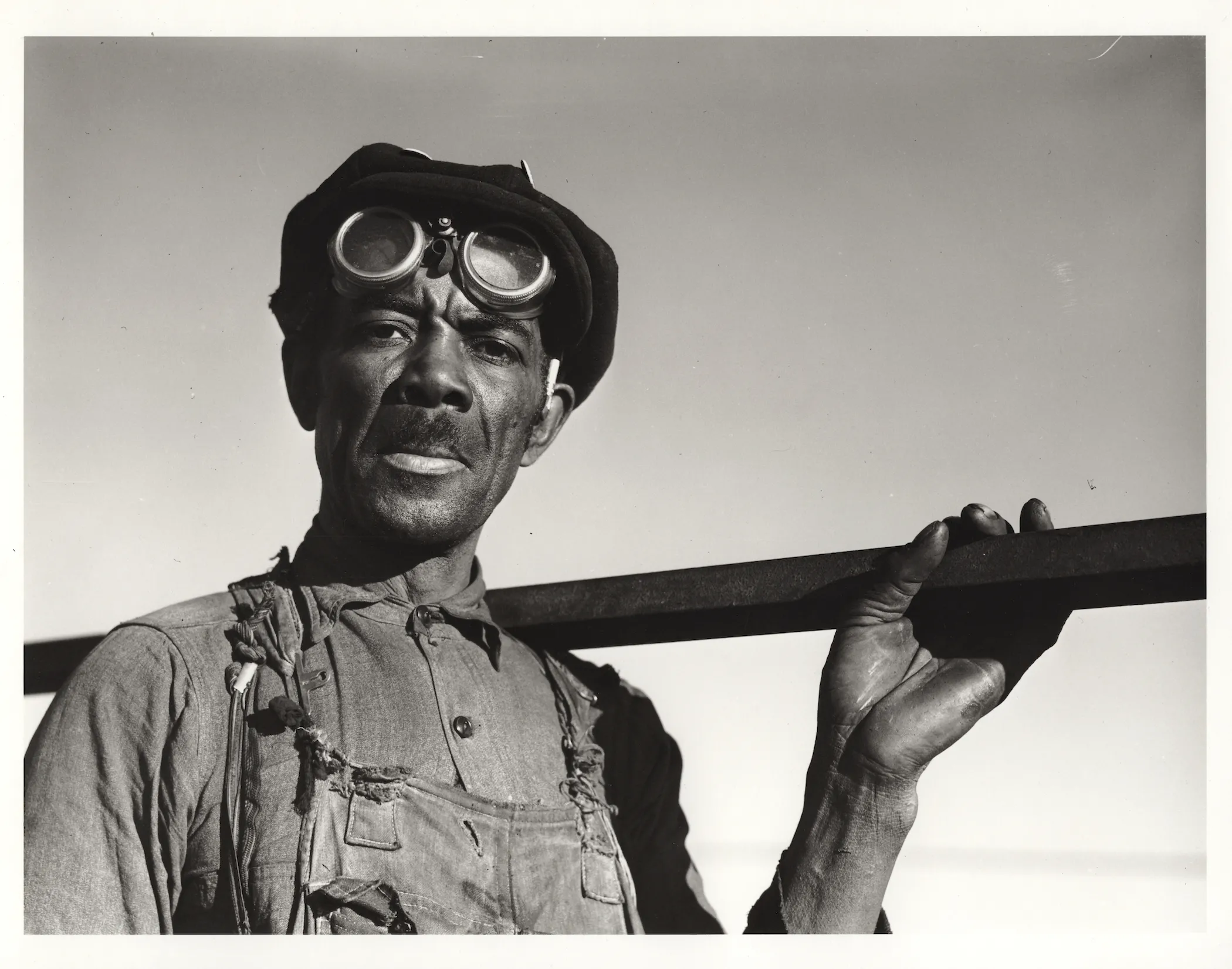 Man with goggles and overalls holding a tool over his shoulder
