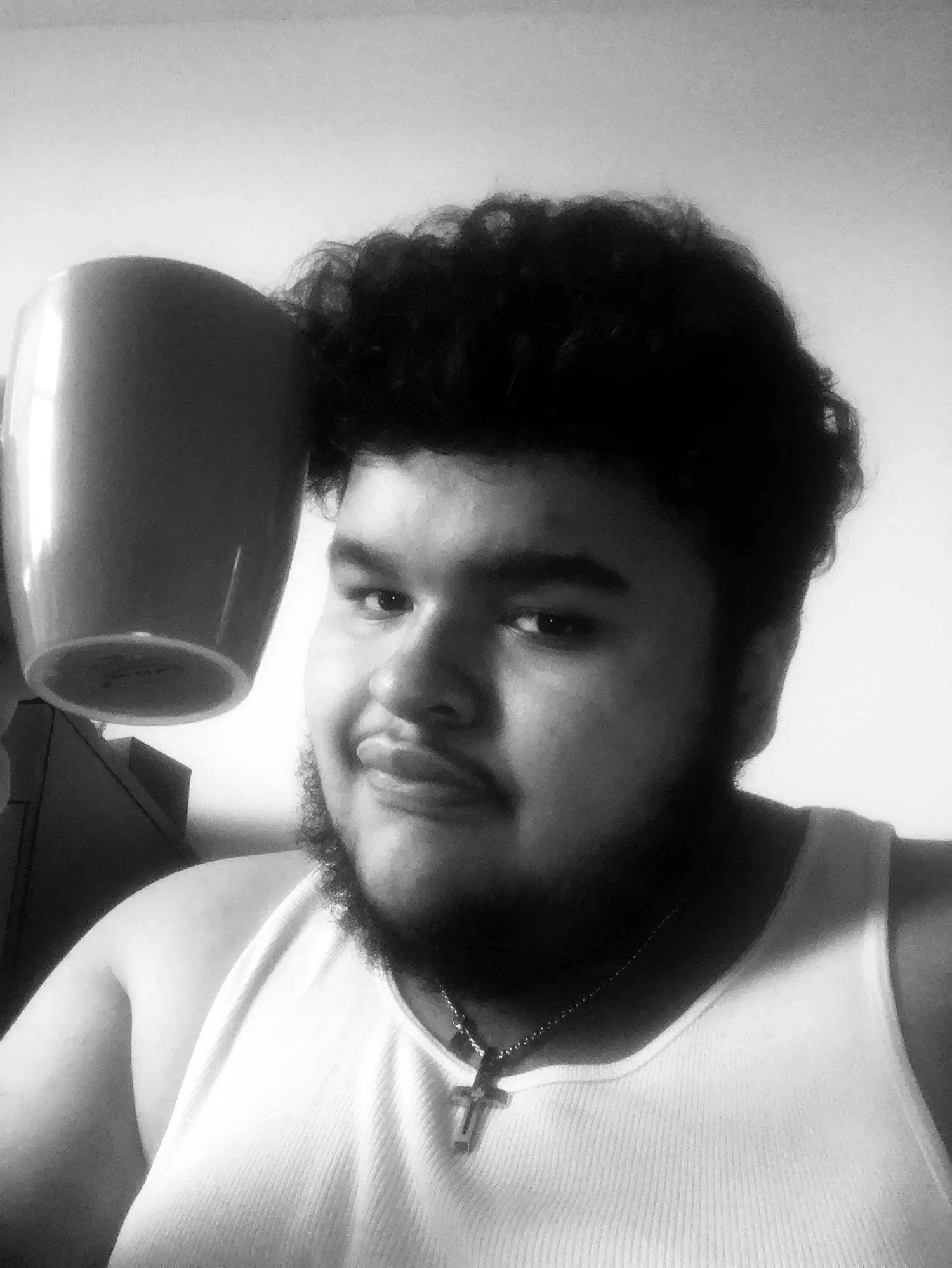 A blurry selfie of somebody in a white undershirt, holding a mug. 