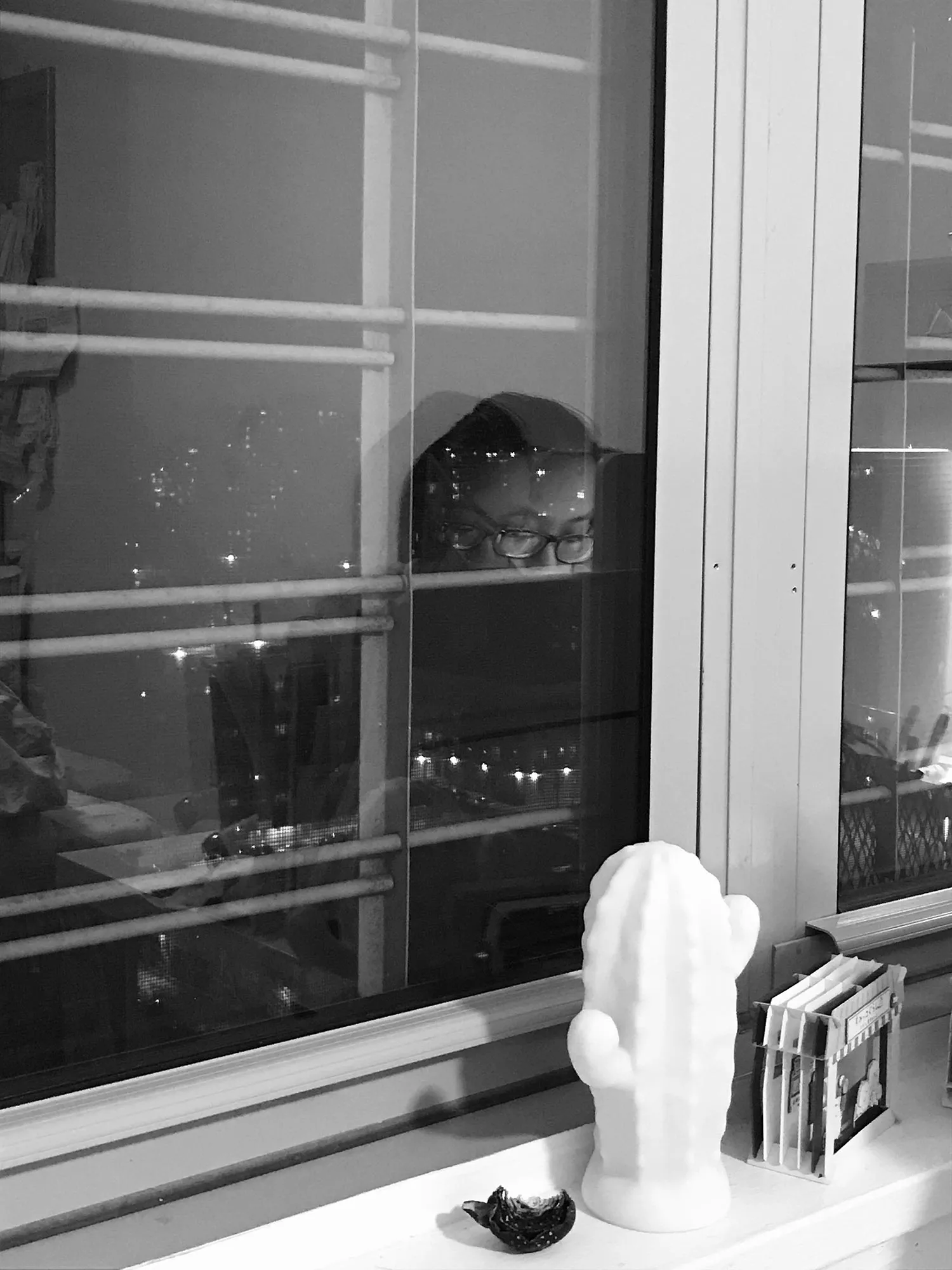 The window's reflection of a woman at her desk. 