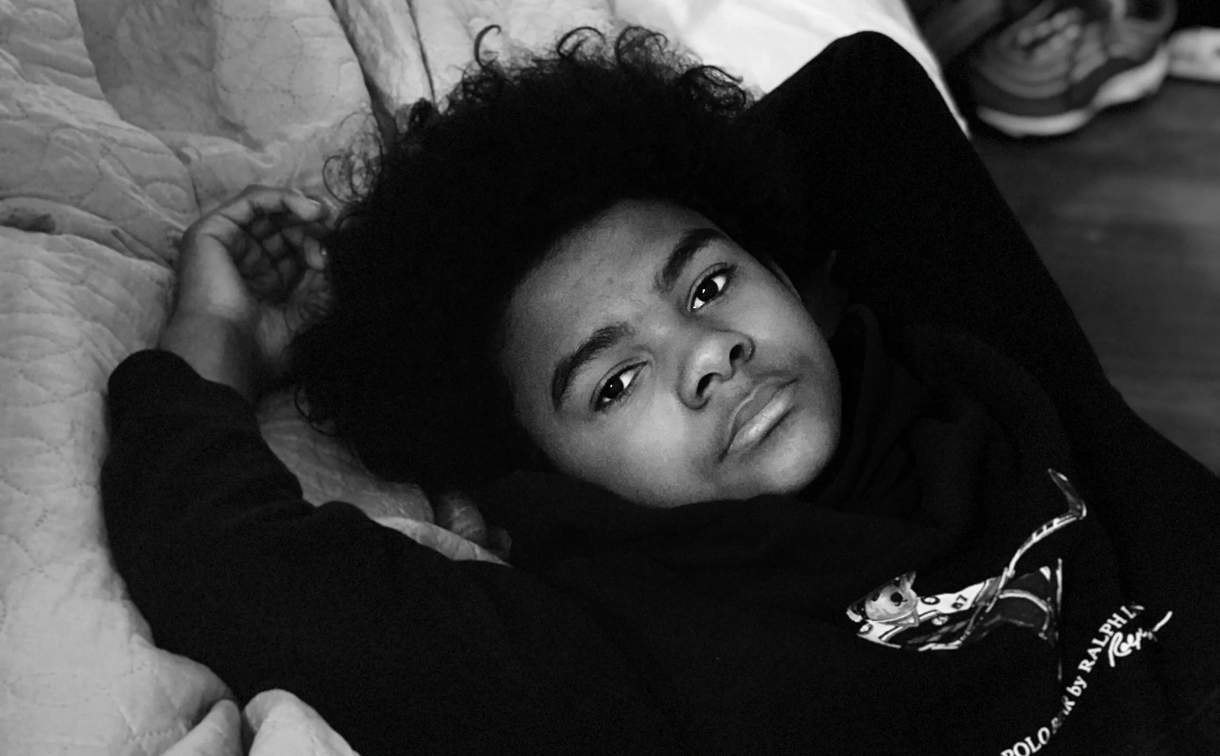 Two children laying in a bed, the younger sister is asleep while the older brother is looking at us.